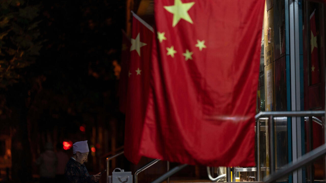 Una anciana se encuentra cerca de las banderas nacionales chinas colgadas para las fiestas del día nacional durante el festival del medio otoño en Beijing, el lunes 6 de octubre de 2025.